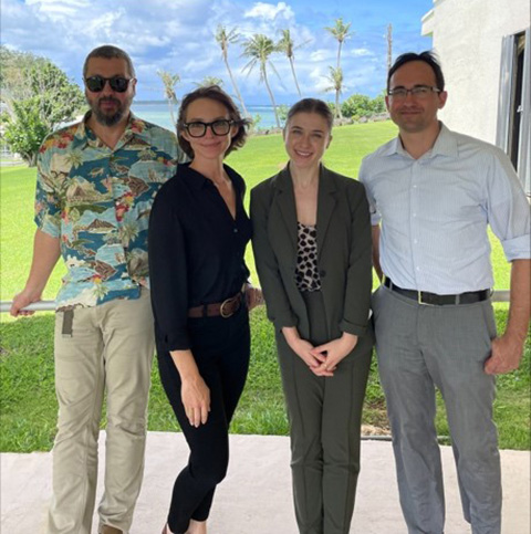 guam-1 Four people under an awning smile in front of green grass and a blue sky.