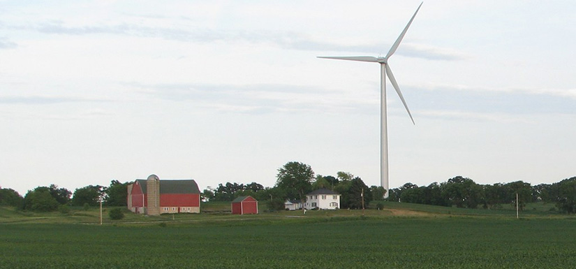 rural-wind-turbine A farm with a barn and farmhouse in a field next to a wind turbine.
