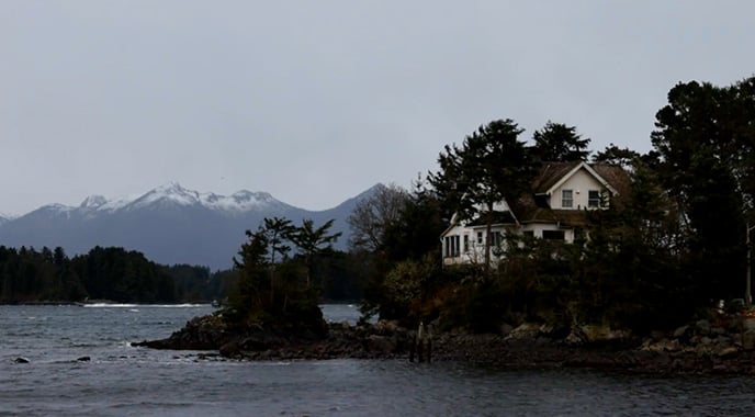 slt-report24-tn A house on a rocky coastline with mountains in the background.