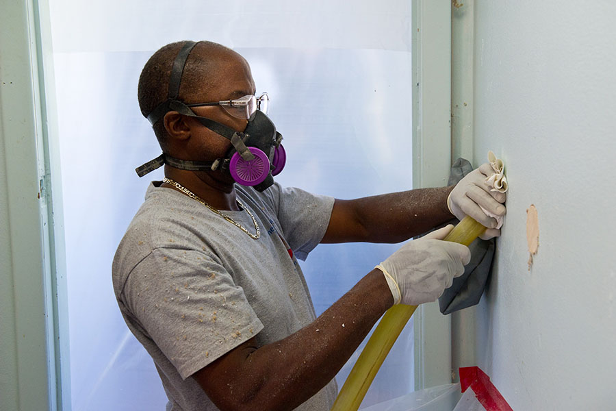 A man wearing a mask holding a tube inside of a wall.