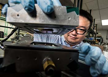 Man wears gloves as he holds two parts of a metal box in a laboratory