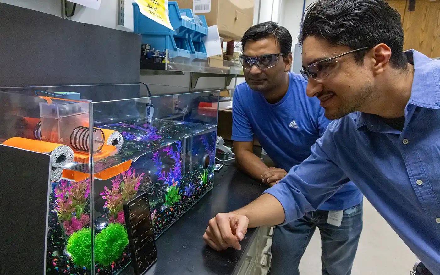 Two men examine a device floating on top of a fish tank.