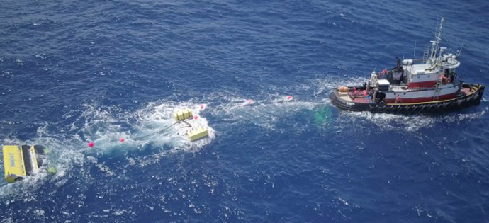 Vessel sails away from marine energy device in ocean.