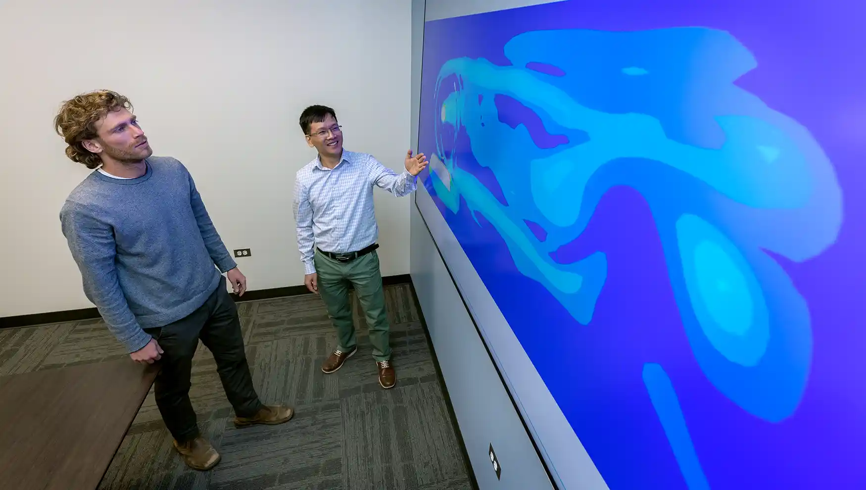 Two researchers looking at a wave model on a large screen.