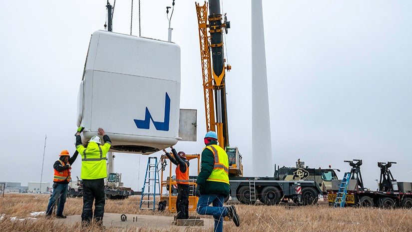 20240125-newsletter-windturbine-removal Crews wearing protective gear position a large wind turbine component being lowered by a crane.