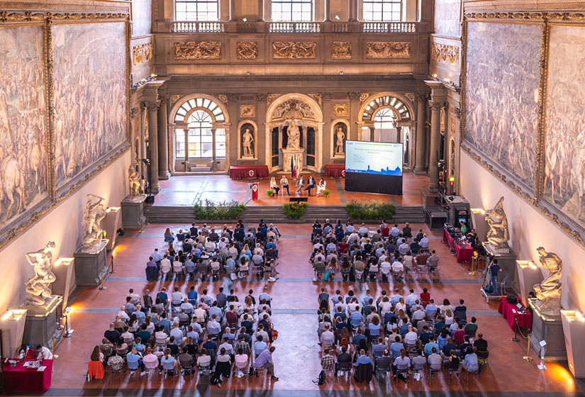 20240723-newsletter-panel Five people sit on a stage with a screen with about 200 people seated on the floor in front of them. Large paintings and sculptures surround the room
