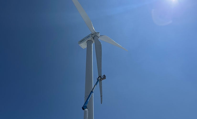 20240723-newsletter-wind-turbine A worker in an extended aerial lift works on the blade of a wind turbine