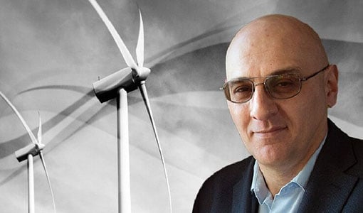 behind-the-blades-vahan Vahan Gevorgian in sunglasses standing in front of solar photovoltaic panels and a wind turbine