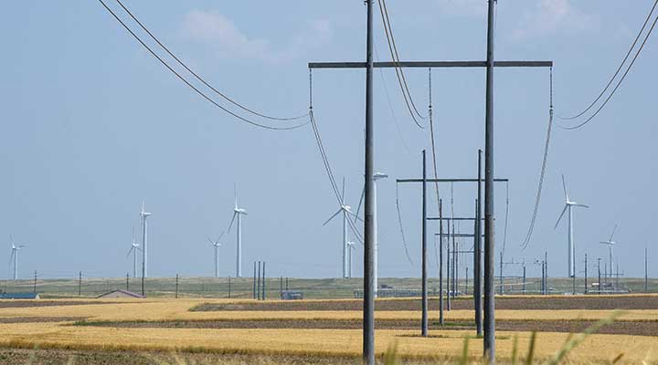 land-based-research-capability-utility-grid-integration A photo of a transmission power line in a brown field with wind turbines in the background.