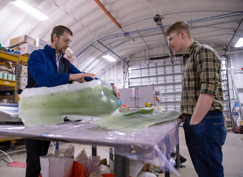 manufacturing-79229 Two people standing over a table, one handling a large object encased in plastic.