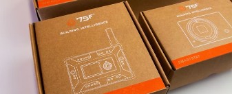 Cardboard boxes bearing images of small device with a screen and reading "75F Building Intelligence."