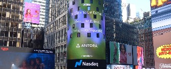 A series of buildings affixed with ads and screens reading "Antora," "NASDAQ," and more.