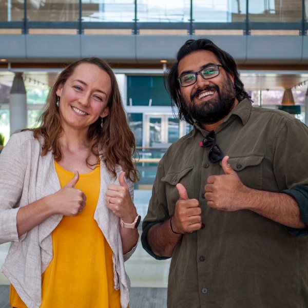 Two people giving thumbs up inside a building's atrium.