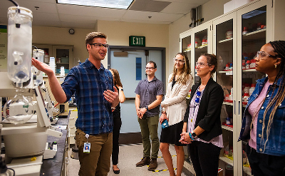 People stand in a lab looking at a man talking