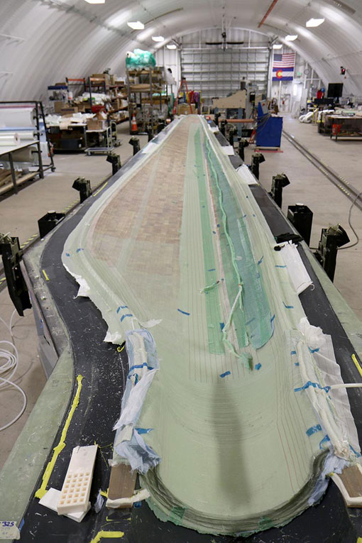 A long, light green component of a turbine blade sits in a white, half-dome facility