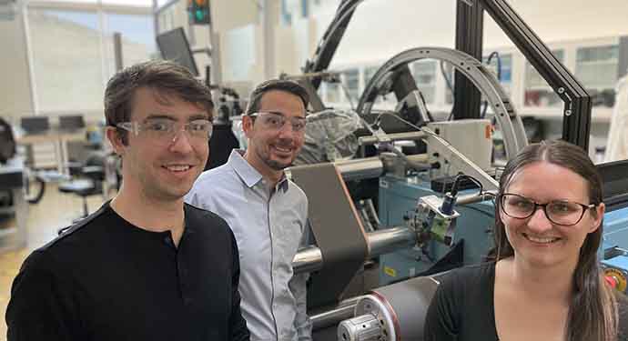 Three researchers in goggles in front of a machine.