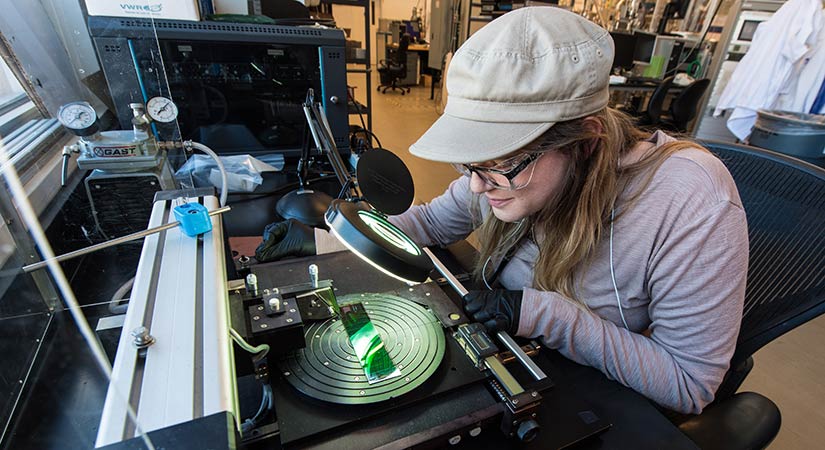NREL scientist looks through a microscope to scribe an organic photovoltaic module in a laboratory setting.