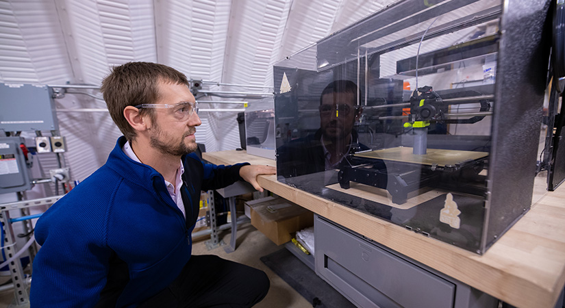 Researcher examines a 3D printer in process.