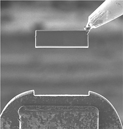 Third of three TEM images showing cutting of trenches to remove a wafer section and transferring that section to a grid post. Here the wafer section is lifted out and seen from the side.