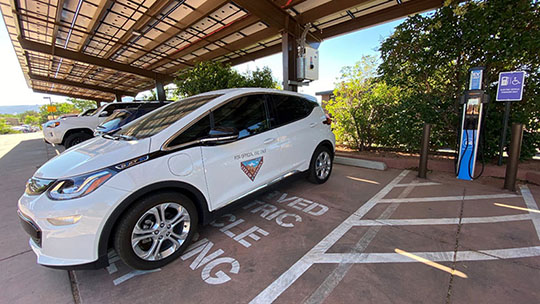 202408-electric-vehicles A white EV, part of a fleet owned by the city of Sedona, parked in a covered parking area.