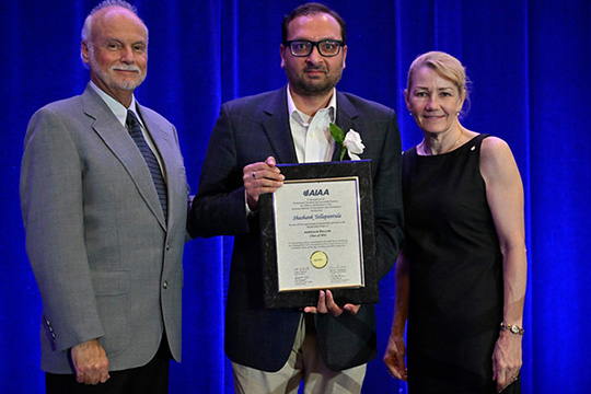 aiaa-fellow-body Three people on a stage, one holding an award.