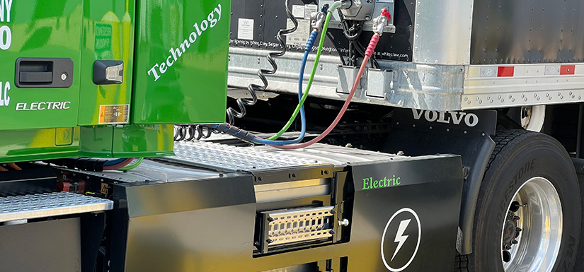 Detail photo of the electrical cables linking a green, 100% electric semitruck cab to its trailer.