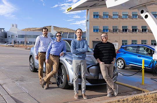 fall24-decades-of-nrel-ev-86268 our people standing around a sedan at a charging station.