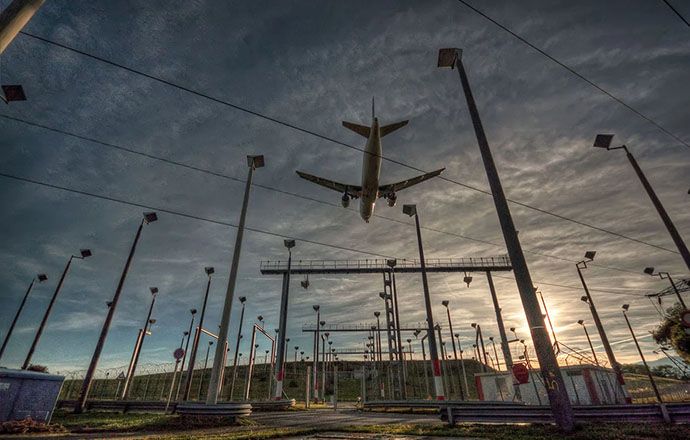 Photo of a large commercial airplane flying over electric infrastructure at an airport.