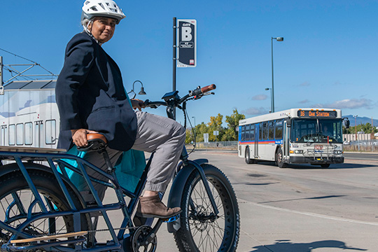 governors-award Woman rides an electric bicycle at the Oak Street RTD rail stop.