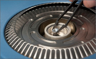 photo_battery_cell Photo of tweezers placing a small round battery cell in the center of a piece of scientific equipment (differential scanning calorimeter).