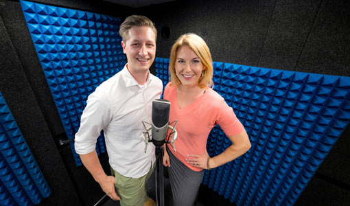 Two people standing side by side in a dark room, smiling