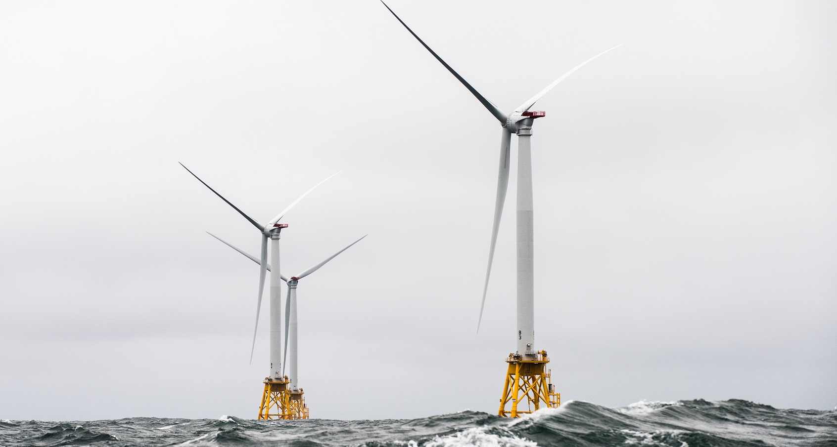 A photo of three offshore wind turbines in turbulent water.