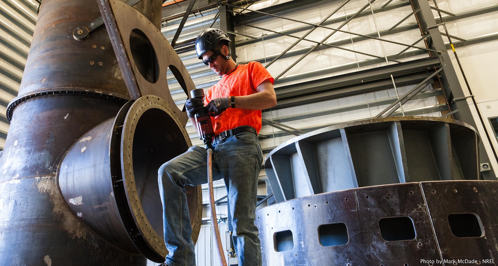 A photo of a man in a hard hat standing next to large machinery.