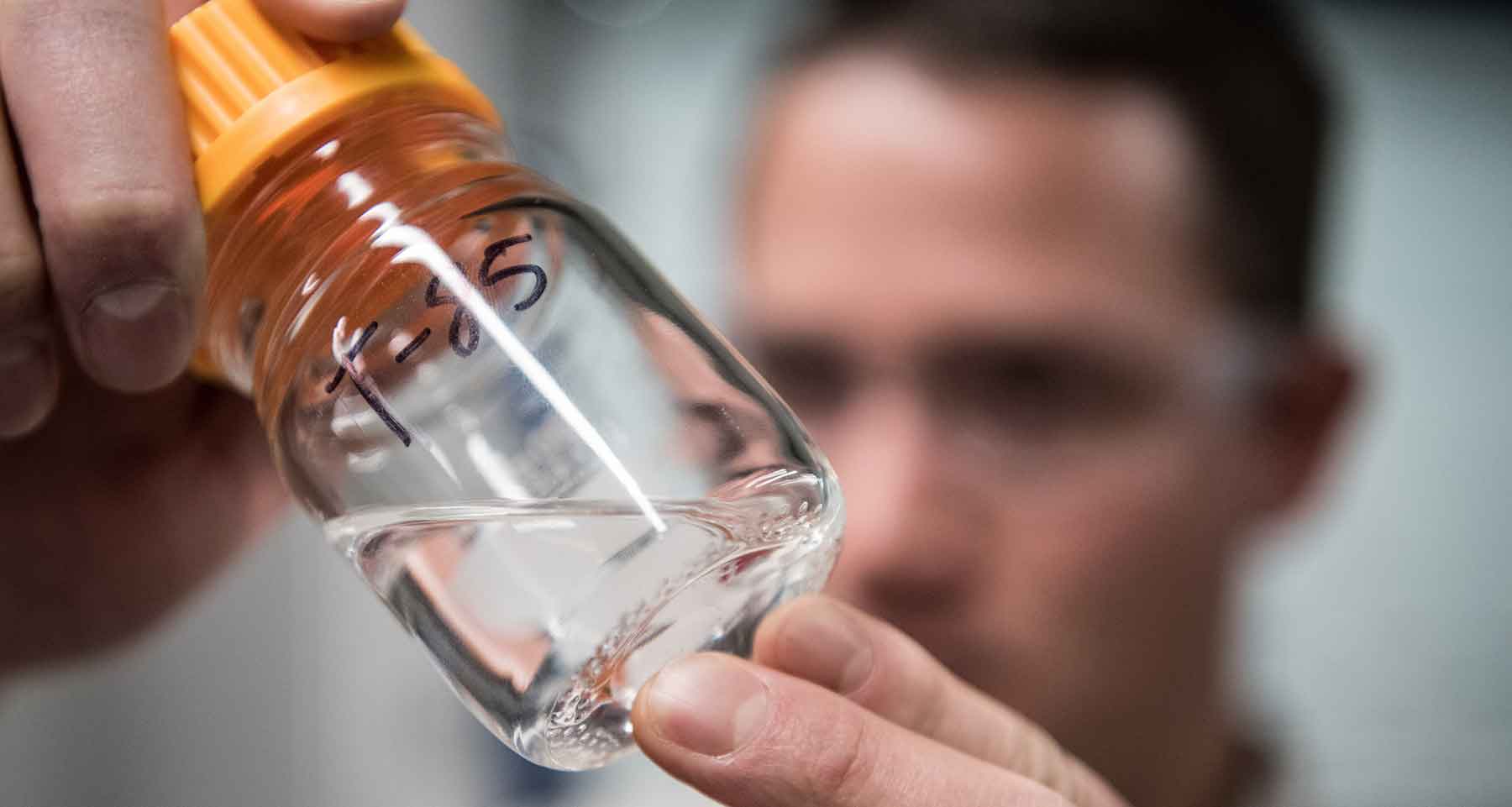 A man holds a bottle containing a clear liquid.