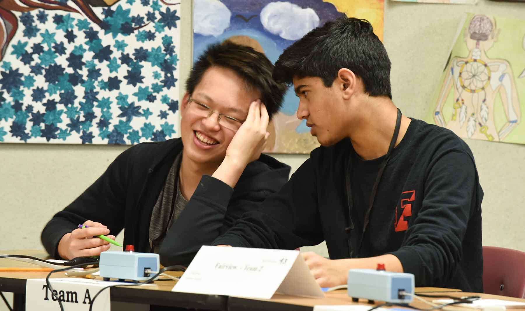 Photo of two students sitting at a desk with competition buzzers.