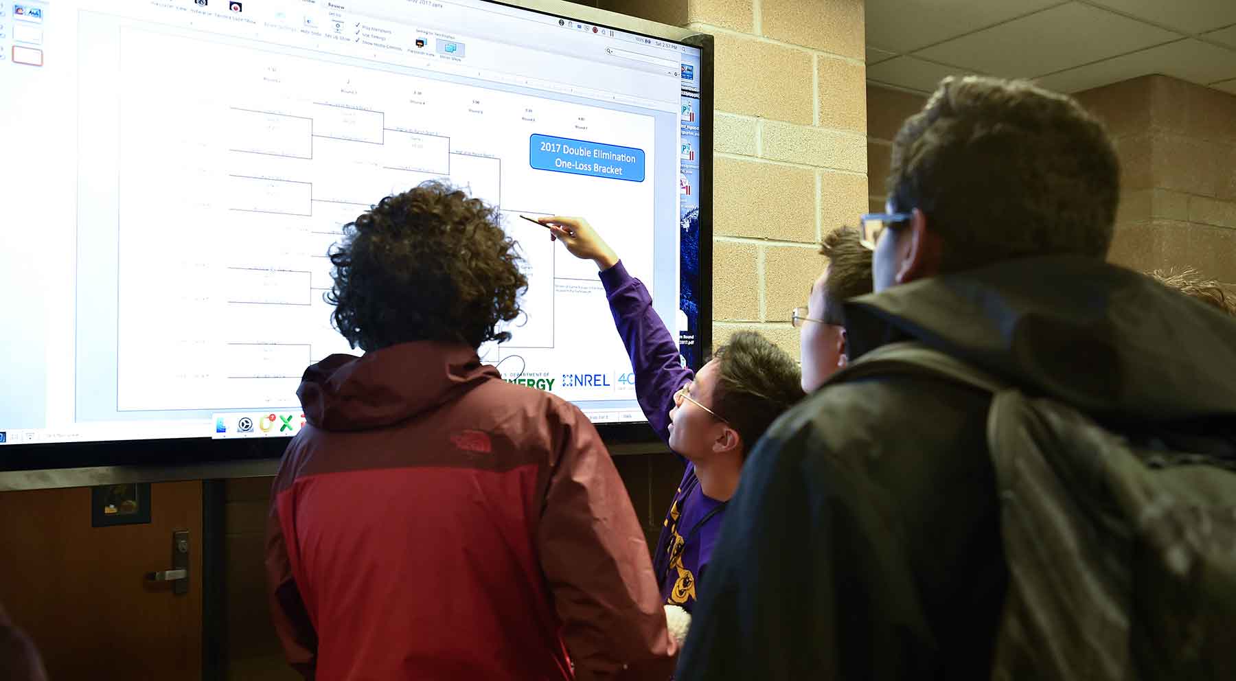 Photo of students looking at and point to a large video monitor.