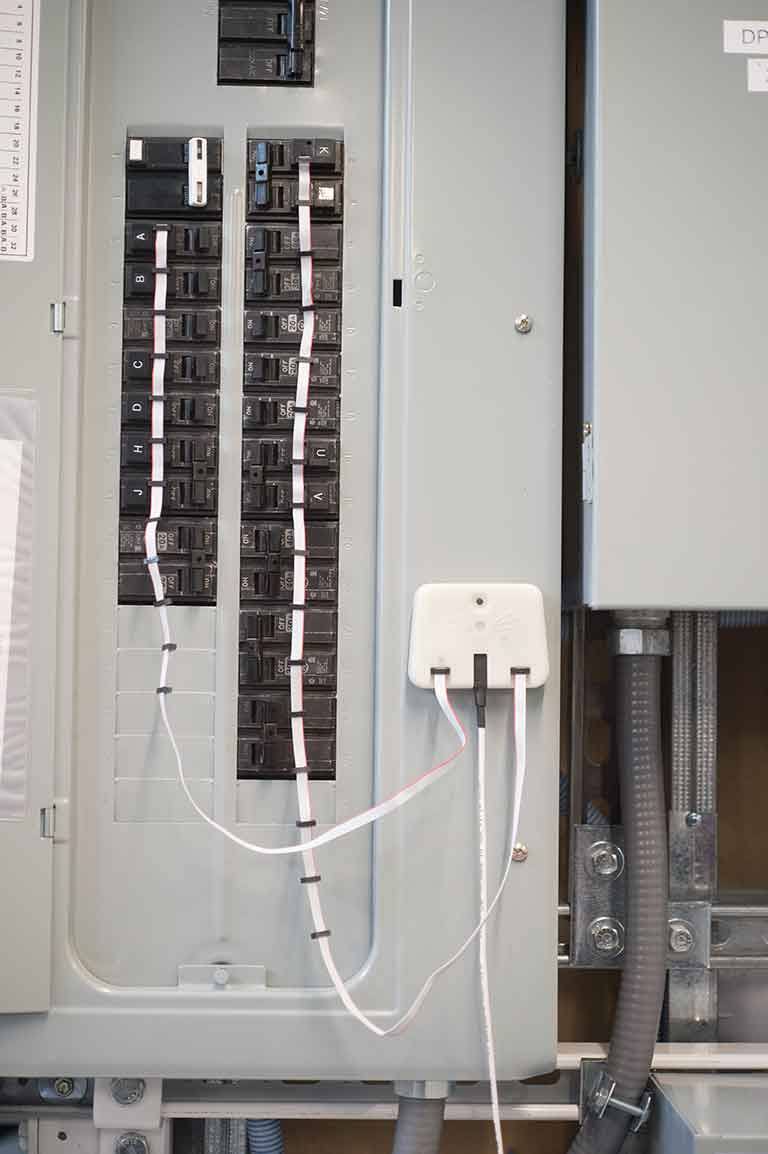 An electric panel with a small, boxy device attached to it by wires.