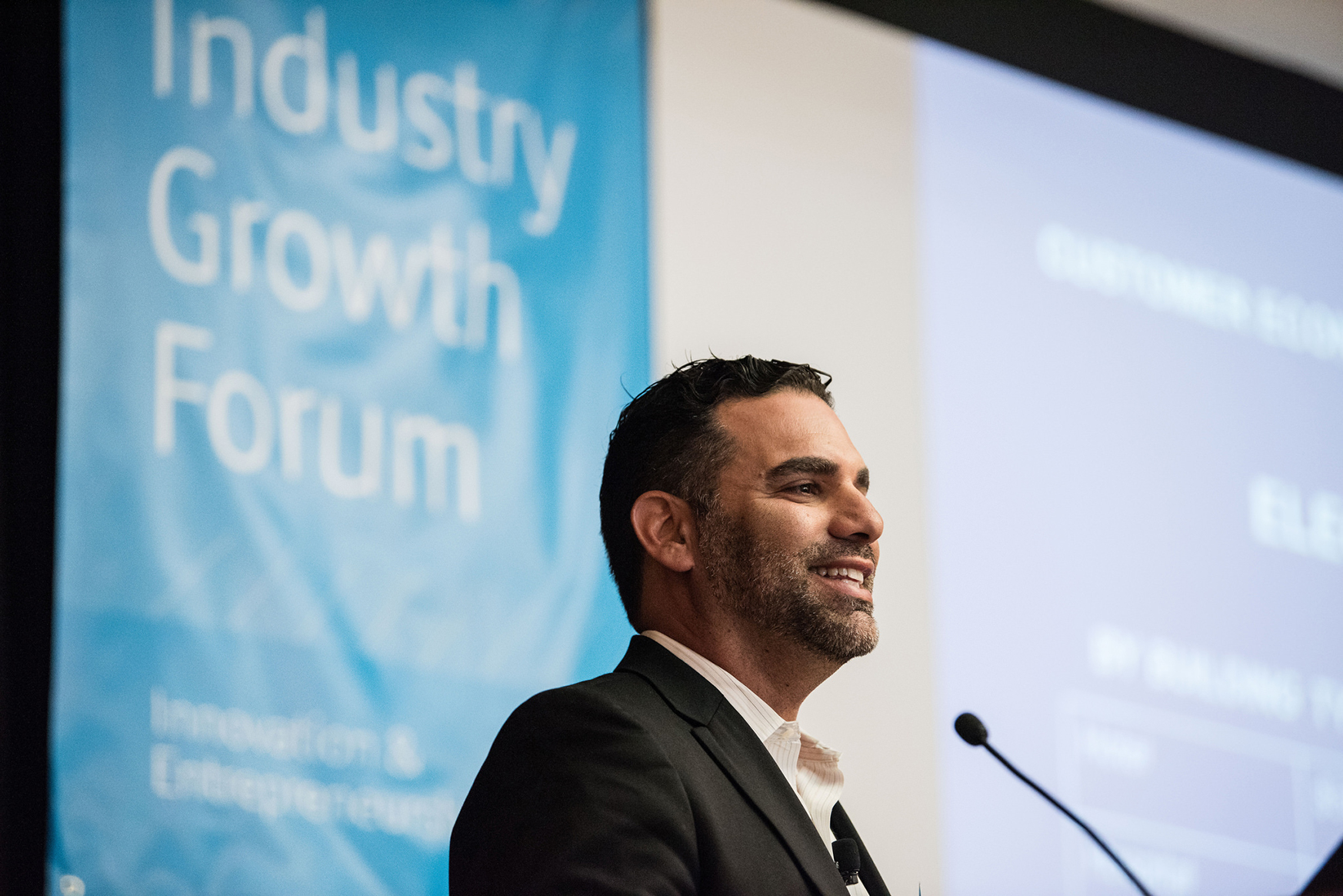 A photo of a man presenting and smiling at a podium.