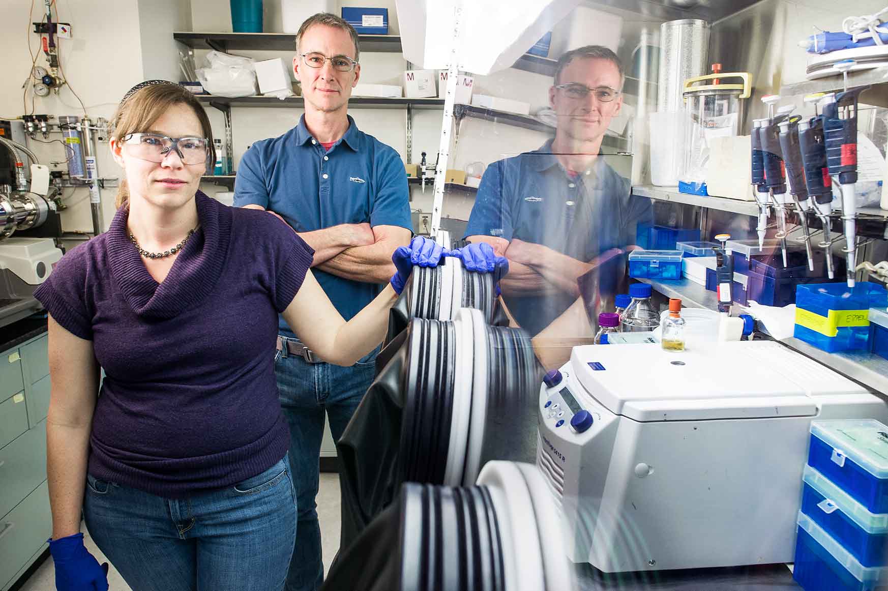 A woman and a man stand next to a piece of equipment in a laboratory setting.