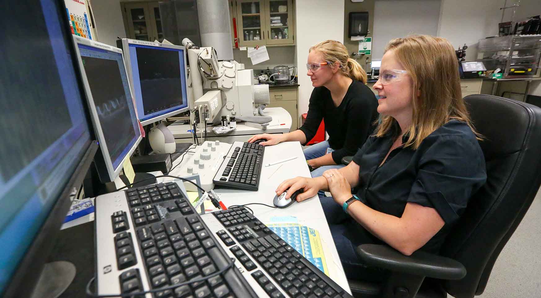 Two women work together at a bank of computer screens in a laboratory.