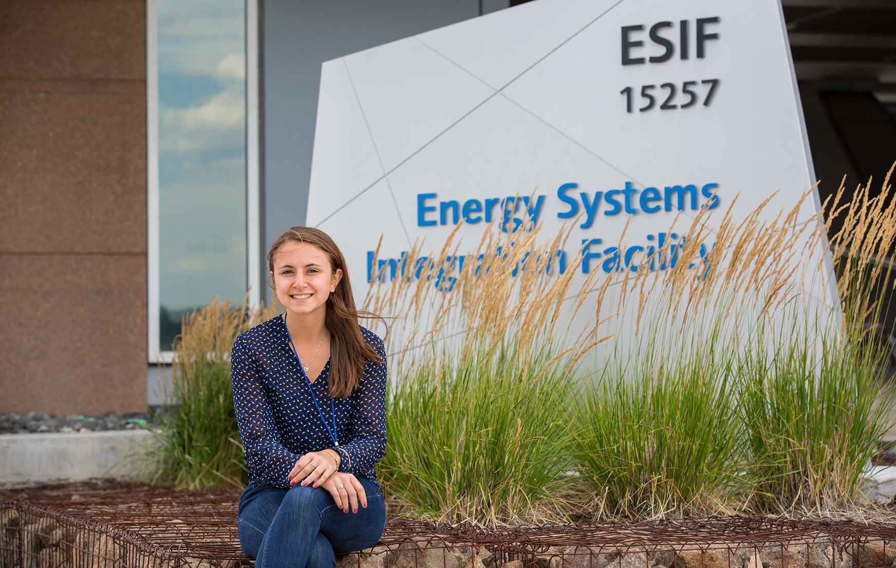 A woman sits in front of a sign that reads “Energy Systems Integration Facility.”