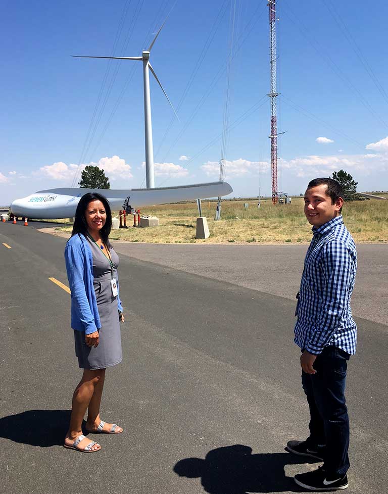 A woman and a man stand in front of a wind turbine.
