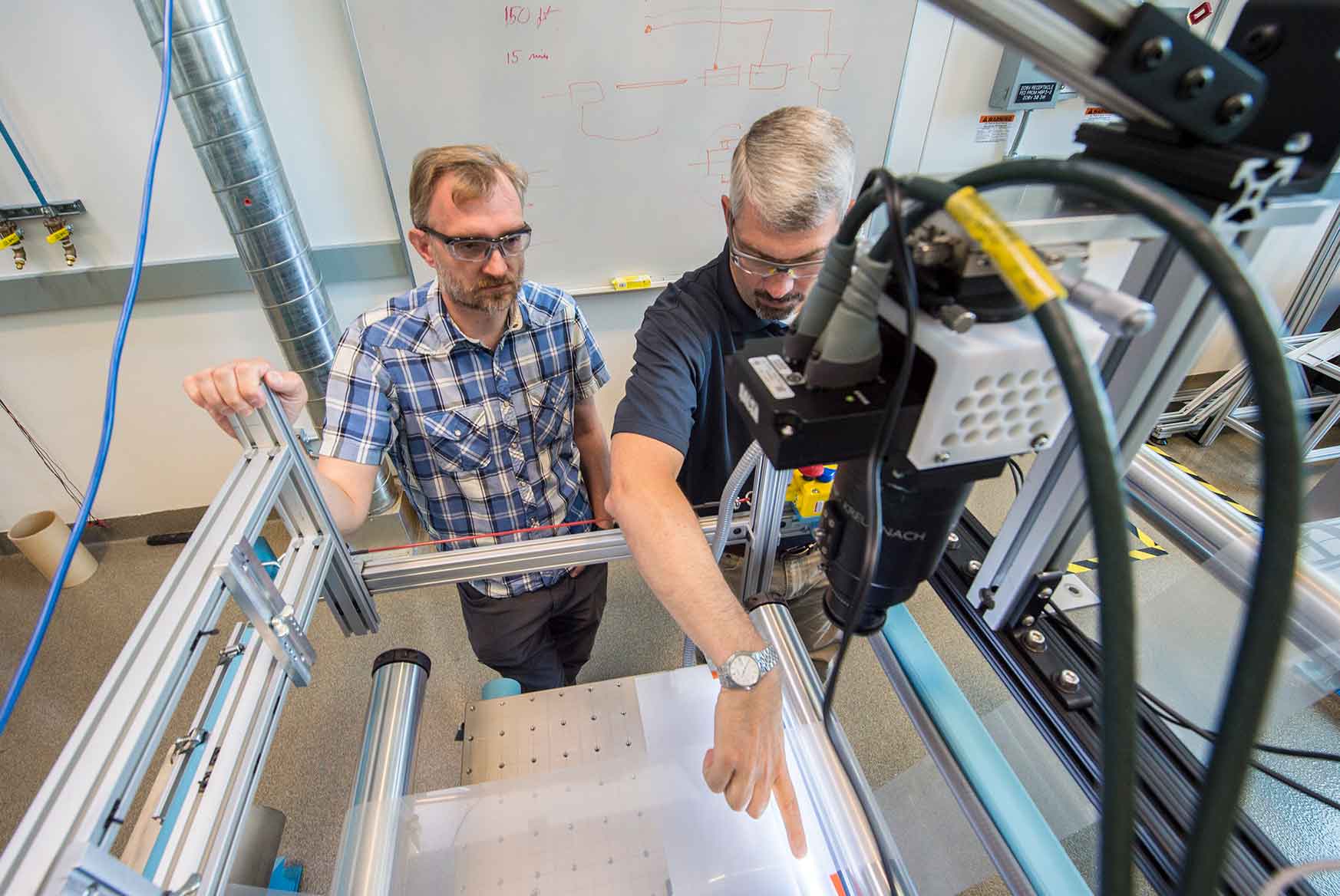 Two men look over a piece of equipment in a laboratory.