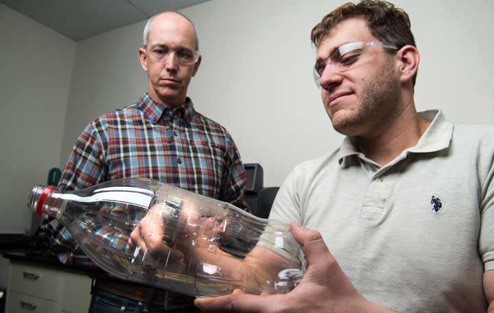 Two men in a lab, one is holding a plastic bottle.