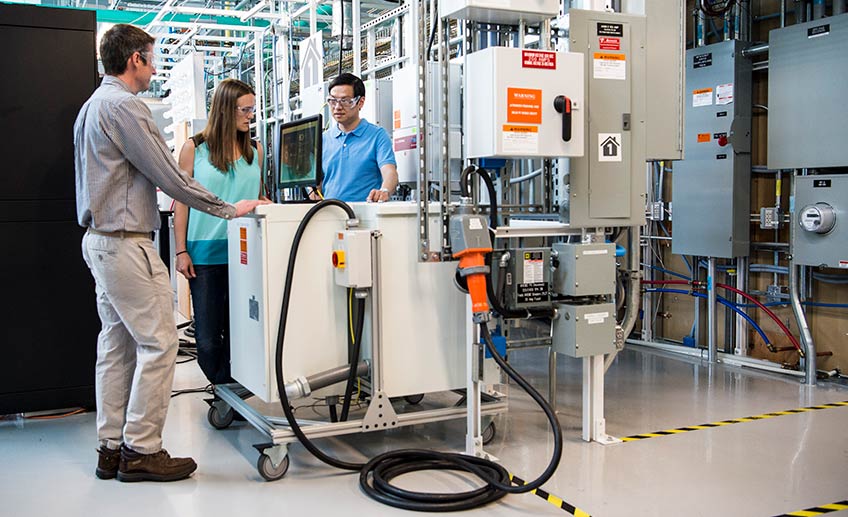 Two men and a woman stand next to a large piece of equipment in a laboratory.