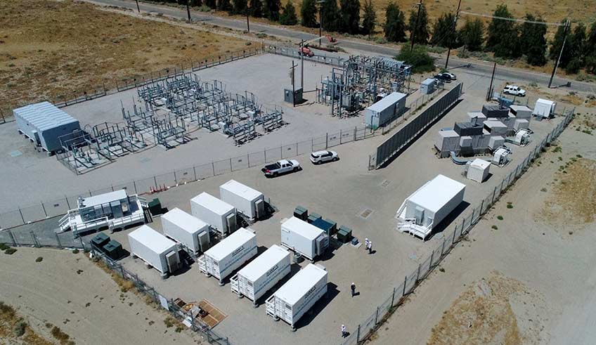 Aerial photo of a microgrid configuration on a cemented area surrounded by brown grass on three sides and a road lined by trees on the fourth side. 