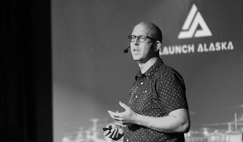 A man stands on a stage and presents to a crowd.