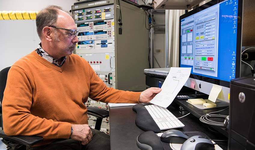 A man looks at a piece of paper while sitting in front of a computer.