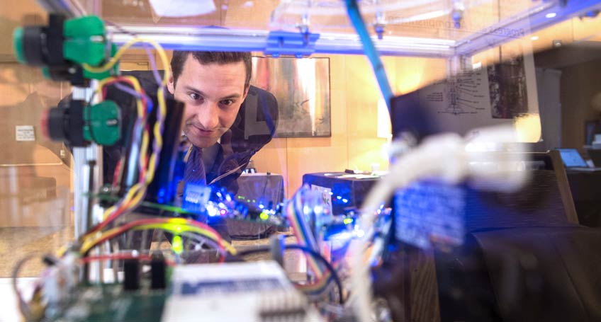 Photo of a man looking into a device surrounded by a clear plastic box.