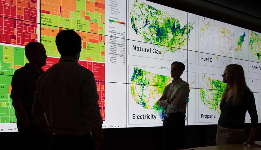 Four people are silhouetted against a giant screen that shows maps of the United States.